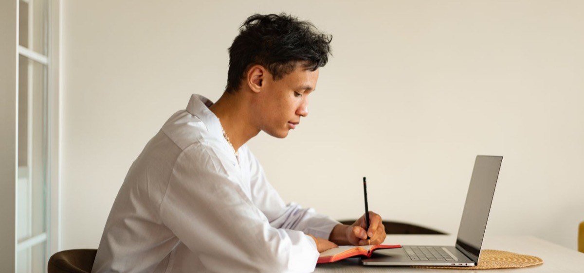 Peserta laki-laki mencatat sambil belajar di depan laptop
